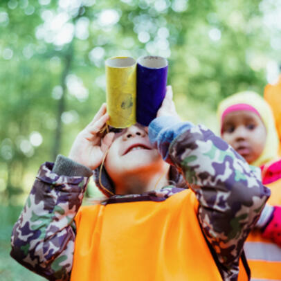 A child is outside, looking at the sky with binoculars they made themselves.