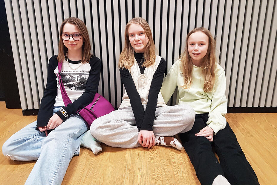 Kolme haastateltua oppilasta istuu lattialla